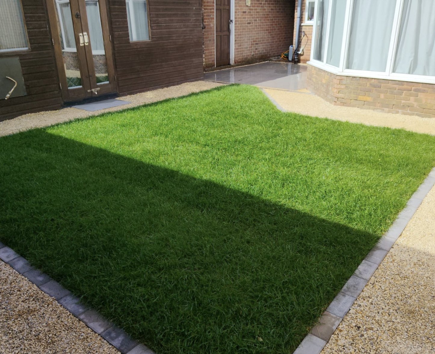 Fresh natural turf lawn with Yorkshire Cream shingle borders beside a conservatory in Lydd by Lawn Ranger Landscapes