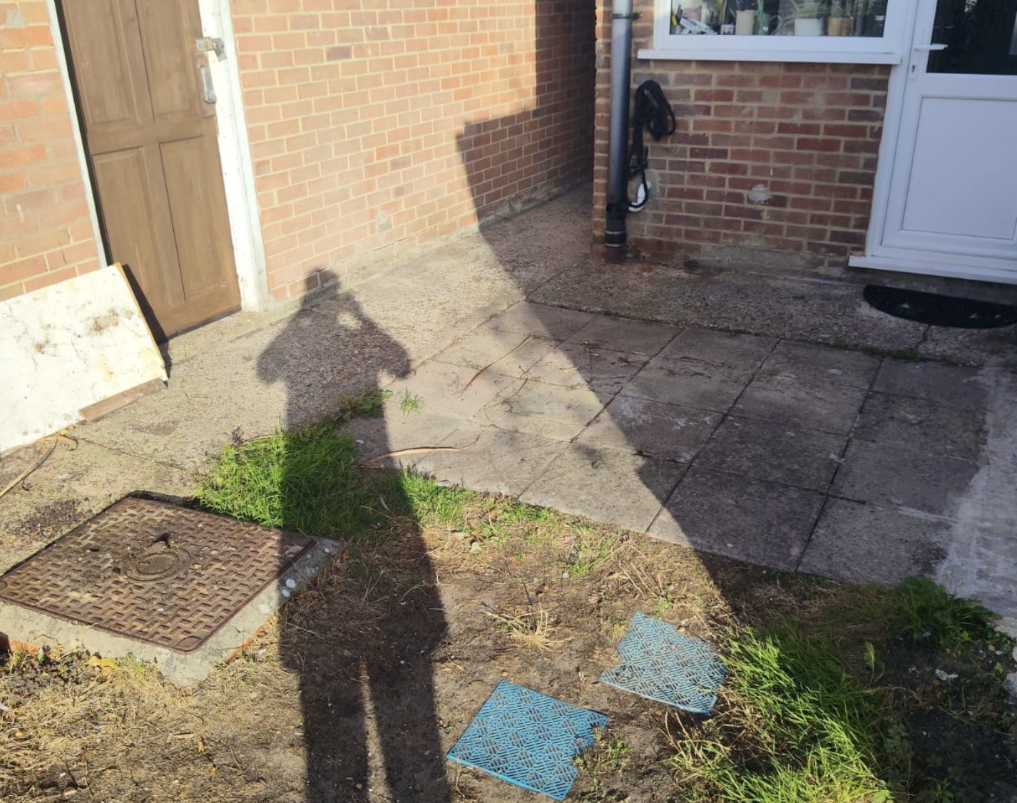 Old worn concrete patio and a raised drain cover before the new porcelain patio in Lydd, Kent